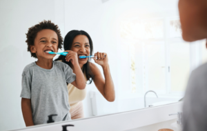 a child and parent smiling and brushing their teeth